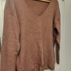 Rosa stickad v-ringad tröja 157 - Mysig stickad tröja i en varm rosa nyans från 157. Tröjan har v-ringning, lång ärm och en lite loose passform. Perfekt för lager-på-lager och chill dagar. Ribbstickade muddar vid ärmslut och nederkant ger en snygg touch.