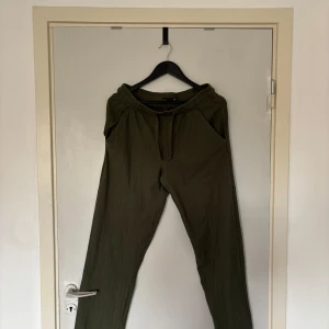 Olivgröna linnebyxor med snörning - Snygga olivgröna linnebyxor i storlek S. Byxorna har elastisk midja med snörning, sidfickor och en bakficka. Perfekta för en chill och avslappnad stil, tillverkade i ett lätt och luftigt linnematerial.
