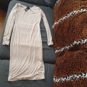 Beige långärmad klänning Boohoo - En stilren beige långklänning från Boohoo med lång ärm och rund halsringning. Klänningen har en tight passform och är tillverkad i ett mjukt bomullsmaterial som känns skönt mot huden. Perfekt för dig som gillar minimalistisk och clean stil.