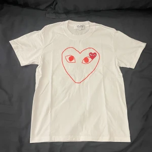 Comme des Garçons T-shirt  - En riktigt snygg vit T-shirt från Comme des Garçons. Med en röd logga på framsidan av tröjan på bröstet. Samt en broderad logga på  vänster sida av bröstet. | Den är så gott som ny i skicket 9,5/10. | Det är bara att höra av sig om man har några frågor🤍🤍🤍
