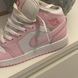 Nike Air Jordan 1 rosa och vita - Snygga Nike Air Jordan 1 sneakers i rosa och vitt med klassisk snörning och ikonisk Air Jordan-logga på sidan. Skorna har en rund tå och är tillverkade i skinn och syntet. Perfekta för dig som vill sticka ut med en fräsch färgkombo.