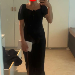 Svart långklänning med puffärm - Supersnygg svart långklänning med puffiga kortärmar och söt snörningsdetalj vid bysten. Klänningen har en figurnära passform och fyrkantig urringning som ger en elegant vibe. Perfekt för dig som vill sticka ut med en klassisk men trendig look.