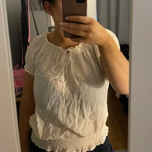 Vit offshoulder blus - Säljer en söt vit offshoulder blus med korta ärmar och knytband framtill. Blusen har en luftig passform och elastiska detaljer vid hals och ärmslut för en bekväm känsla. Storlek M men passar också S