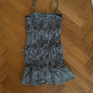Svartvit rutig mini-dress från Bershka💕 - Snygg svartvit rutig klänning från Bershka med smala axelband och volangdetaljer. Perfekt för en festlook🥳🥂 Klänningen har en kort längd och är tillverkad i ett lätt material💕💕
