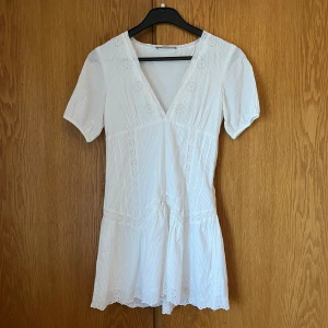 Vit kortklänning från Zara - Säljer en söt vit kortklänning från Zara med v-ringning och korta ärmar. Klänningen har fina spetsdetaljer och ett diskret randigt mönster. Perfekt till sommaren och studenten!❤️