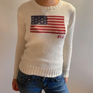 Vit stickad ralph lauren tröja - Säljer en jätte snygg ralph lauren tröja med med en stor amerikansk flagga på bröstet. Tröjan har långa ärmar och ribbstickade muddar vid ärmslut och nederkant. Det är några sminkfläckar på kragen men det är inget som syns💓
