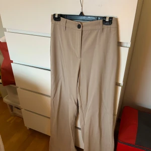 Beige kostymbyxor från Bershka - Snygga beige kostymbyxor från Bershka som är raka och lite vida. Byxorna är sjukt bekväma och snygg beige färg! Sparsamt använda, storlek 38! Jag är 163cm!