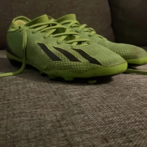 Gröna fotbollsskor från Adidas - Snygga gröna fotbollsskor från Adidas med svarta detaljer och snörning. Perfekta för fotbollsplanen med sina robusta dobbar för bra grepp.