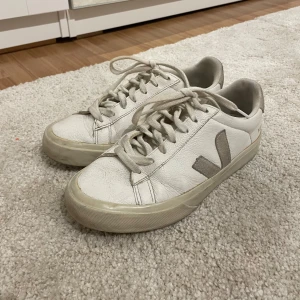 Vita sneakers från Veja - Säljer ett par vita sneakers från Veja med beige detaljer. Skorna har snörning och är sköna att gå i så de funkar bra till vardags. Sparsamt använda men en aning slitna och lite smutsiga men annars i mycket bra skick. Nypris ca 1650kr💕 