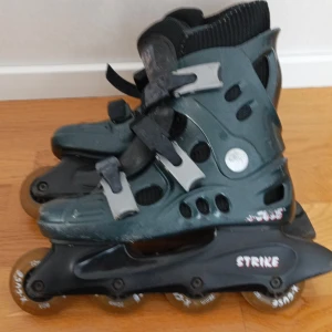 Svarta inlines från Strike - Säljer ett par svarta inlines från Strike med justerbara spännen och robusta hjul. Perfekta för en tur i parken eller längs strandpromenaden. De har en stabil konstruktion och bekväm passform.