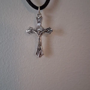 Silverfärgat korshalsband - Snyggt silverfärgat korshalsband med detaljerad design. Hängs på en svart snodd vilket ger en stilren kontrast. Perfekt för att ge en personlig touch till din stil.