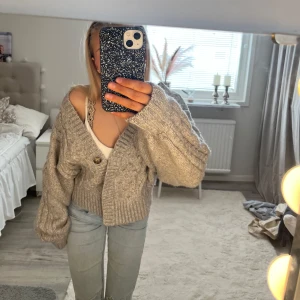 Grå stickad kofta med knappar - Säljer en mysig grå stickad kofta med flätmönster och stora knappar. Koftan har en croppad passform och långa ärmar. Den ribbade kanten ger en extra touch av stil. Passar utmärkt till jeans. Tröjan är i storlek M! Hör av dig vid intresse💞