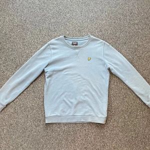 Grå sweatshirt från Lyle & Scott - Säljer en stilren torkås blå  sweatshirt från Lyle & Scott med deras ikoniska gula logga på bröstet. Tröjan har långa ärmar och en rund halsringning. Perfekt för en avslappnad stil.