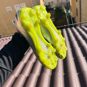 Fotbollsskor med neongula dobbar - Säljer ett par fotbollsskor med neongula dobbar och grå ovandel med svarta detaljer. Skorna har snörning och är perfekta för fotbollsplanen. De har en modern design som sticker ut.