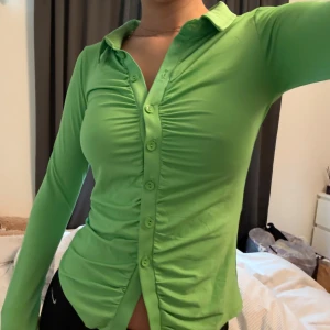 Grön topp med krage från Nelly - Snygg grön topp med krage från Nelly. Toppen har långa ärmar och knappar framtill. Den är figurnära och har en stilren design som passar perfekt för olika tillfällen.