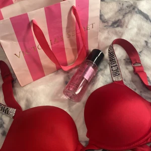 Röd bh med strassdetaljer från Victoria's Secret - Påse och parfymen ingår Snygg röd bh från Victoria's Secret med glittriga strassdetaljer på axelbanden. Perfekt för att lägga till lite glamour i vardagen. Inkluderar en doftmist 'Pure Seduction' för en komplett look.