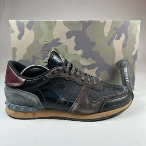 Valentino Rockrunner i kamouflage - Snygga Valentino Rockrunner sneakers i en cool kamouflage-design. Skorna har en mix av svart, grå och brun färg med detaljer i mocka och skinn. Storlek 43 men passar 44 Original box och snören medföljer. Perfekta nu till sommaren.