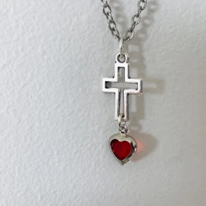 Silverhalsband med kors och rött hjärta - Elegant silverhalsband med ett korshänge och ett rött hjärta. Perfekt för att ge en stilfull touch till din outfit. Kedjan är tunn och smidig, vilket gör den bekväm att bära hela dagen.