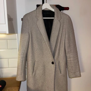 Beige kappa från Zara - Säljer en stilren beige kappa från Zara. Den har en klassisk design med en enkel knapp framtill och två fickor. Perfekt vårkappa!✨