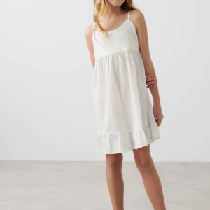 Vit ärmlös klänning med volang - Säljer en söt vit klänning i linne med smala axelband och volangdetalj vid fållen. Perfekt för varma sommardagar med sin luftiga och bekväma passform.