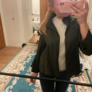 Grön jacka med knappar - Snygg grön jacka med knappar framtill. Den har en hög krage och långa ärmar. Perfekt för en stilren look.