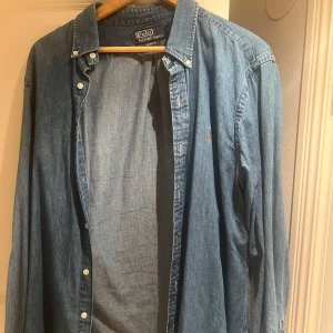 Blå skjorta från Polo Ralph Lauren - Snygg blå skjorta från Polo Ralph Lauren med klassisk krage och knappar framtill. Perfekt för en avslappnad stil. Skjortan har långa ärmar och en liten broderad logga på bröstet.