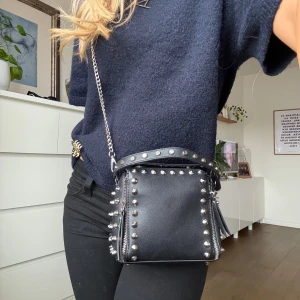 Svart axelväska med nitar - Snygg svart väska i skinn med coola nitar runtom. Den längre kedjan går att ta av! Dragkedjorna är både prydnad men gör även att det facket blir större❤️‍🔥 Perfekt för att ge din outfit en snygg touch❣️Se bild 4 för defekt!