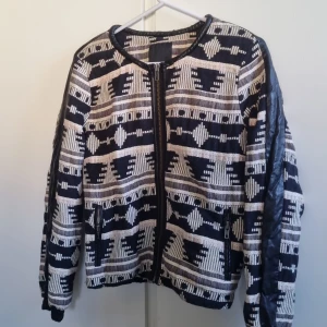 Mönstrad jacka med dragkedja - Snygg jacka med ett unikt geometriskt mönster i svart och beige. I fint skick.