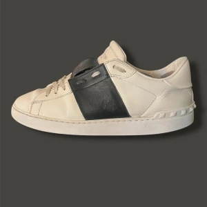 Valentino Garavani sneakers - Snygga Valentino Garavani sneakers i vitt med svart detalj. Skorna har en klassisk design med snörning och är tillverkade i skinn. Perfekta för en stilren look.