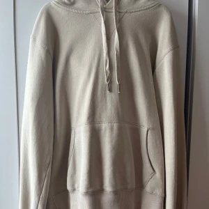 Beige hoodie från Cubus - Säljer en stilren beige hoodie från märket Cubus. Den har en klassisk design med en stor ficka framtill och justerbar huva med dragsko. Perfekt för en avslappnad look.