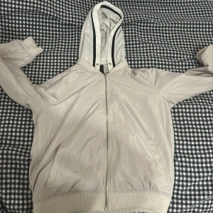 Beige vindjacka från FB Sister - Säljer en beige vindjacka från FB Sister med huva och dragkedja. Jackan har ribbade muddar och en stilren design. Perfekt för vår och höst!