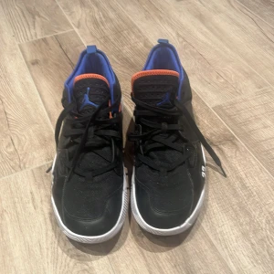 Svarta Nike Air Jordans med blå och orange detaljer - Säljer ett par svarta Nike Air Jordans med coola blå och orange detaljer. Skorna har snörning och en vit sula med nummerdetalj bak. Perfekta för dig som vill ha en sportig och stilren look.(priset kan diskuteras)