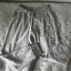 Grå mjukisbyxor från Hollister - Snygga grå mjukisbyxor från Hollister med snörning i midjan och ribbade muddar vid bensluten. ‼️‼️köpt från vinted, sa att de var helt nya, men man ser att de är använda, har en liten fläck som säkert går bort i tvätten, syns knappast, sen är den lite noppig på ett ställe. passar inte på 168cm+