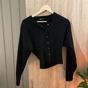 Svart kofta från Gina Tricot - Snygg svart kofta från Gina Tricot med knappar framtill. Perfekt för lager-på-lager och att hålla sig varm under kyligare dagar. Enkel och stilren design som passar till det mesta.