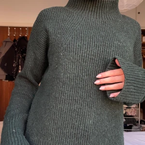 Mörkgrön stickad polotröja - Säljer en mysig mörkgrön stickad polotröja med ribbad design. Tröjan har långa ärmar och en hög krage som håller dig varm under kyliga dagar. Perfekt för höst och vinter!
