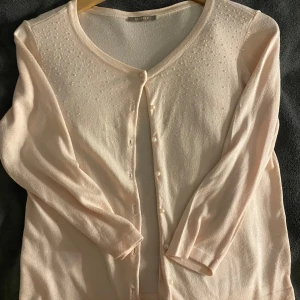 Ljusrosa kofta med trekvartslångaärmar - Säljer en söt ljusrosa kofta från Orsay med pärldetaljer på axlarna. Koftan har trekvartslånga ärmar och knäpps med små knappar framtill. Perfekt för en elegant touch till din outfit! 💖