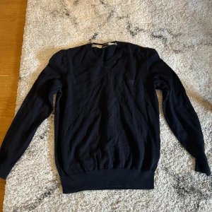Svart stickad tröja från hugo boss - En klassisk svart stickad tröja från boss med rund halsringning och diskret logga på bröstet. Tröjan har långa ärmar. Lite liten i storlek 