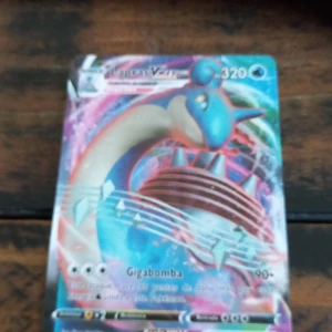 Pokémonkort - Dracovish VMAX - Säljer ett Pokémonkort med Dracovish VMAX. Kortet har färgstark design med blå, röd och vit färg och visar Dracovish i dynamisk pose. Texten på kortet är på spanska och det är en VMAX-version med 320 HP.