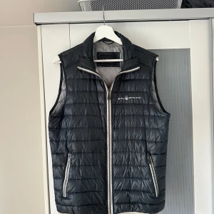 Väst dunväst från Sail Racing - Mörkblå väst från Sail Racing med dragkedja framtill och två fickor med dragkedja i gott skick. Öppen för bud!