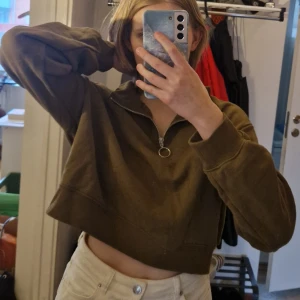 Olivgrön croppad sweatshirt med dragkedja från H&M  - Säljer en olivgrön croppad sweatshirt från H&M Divided med halv dragkedja och ringdetalj. Tröjan har långa ärmar, ribbade muddar och en avslappnad passform. Skriv vid frågor!✨️ Samfraktar gärna så kika in mina andra inlägg!✨️