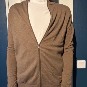 Brun ziptröja från Selected Homme - Säljer en brun ziptröja från Selected Homme. Tröjan har dragkedja framtill, ribbade muddar och är tillverkad i mjukt material. Perfekt för lager-på-lager och enkel att matcha med olika outfits.