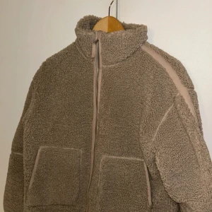 Beige teddyjacka från H&M - Mysig beige teddyjacka från H&M med hög krage och dragkedja framtill. Jackan har två stora fickor och är fodrad på insidan. Knappt använd!💗