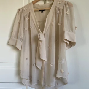 Beige blus från Topshop - Fin beige blus från Topshop med dekorativa blommor och knytning, genomskinlig material.🤎Person på bild är 160cm och brukar ha storlek 36-38. Fint skick. 