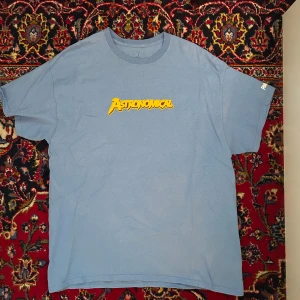 Blå Astronomical x Fortnite t-shirt från Cactus Jack - Säljer en blå t-shirt från Cactus Jack x Fortnite med 'Astronomical' tryck på bröstet och Fortnite-logga på ärmen. Stor färgglad vapen-grafik på ryggen. 100% bomull, relaxed fit och perfekt för gaming eller streetwear. Travis Scott.