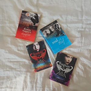 The Demon Trappers Series av Jana Oliver - Fyra böcker ur The Demon Trappers-serien: 'The Demon Trapper's Daughter', 'Soul Thief', 'Foretold' och 'Forgiven'. Böckerna har färgstarka omslag i rött, blått, svart och lila med fantasyinspirerade illustrationer och titlar i stora bokstäver.