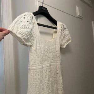 Vit stickad klänning från ZARA - Superfin vit stickad klänning från ZARA med korta puffärmar och rund halsringning. Klänningen har ett vackert virkat mönster och är perfekt för sommarens alla tillfällen. Lätt och luftig modell som ger en romantisk känsla.