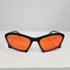 Bruna solglasögon med orange glas - Snygga solglasögon med brun båge och coola orangefärgade glas. Bågarna har en sportig, kantig design som ger en futuristisk vibe. Perfekta för dig som vill sticka ut med en unik accessoar.