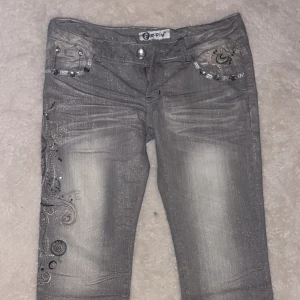 Lågmidjade jeans🪩 - Säljer ett par grå jeans med glittrig finish och dekorativa paljetter samt broderier på fickor och ben. Byxorna har normal passform och dragkedja framtill. Pris går att diskutera🪩💋