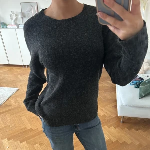 Mörkgrå stickad tröja - Säljer en enkel och stilren mörkgrå stickad tröja med rund halsringning. Tröjan har lång ärm och en klassisk passform som funkar till det mesta. Perfekt för kyligare dagar.