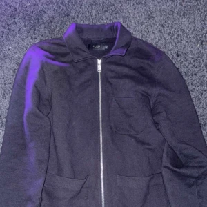 Marin blå overshirt med dragkedja från Riley - Säljer en marin blå overshirt från Riley med dragkedja framtill och klassisk krage. Overshirten har två fickor nertill och en bröstficka. Enkel och stilren design som passar till många tillfällen.
